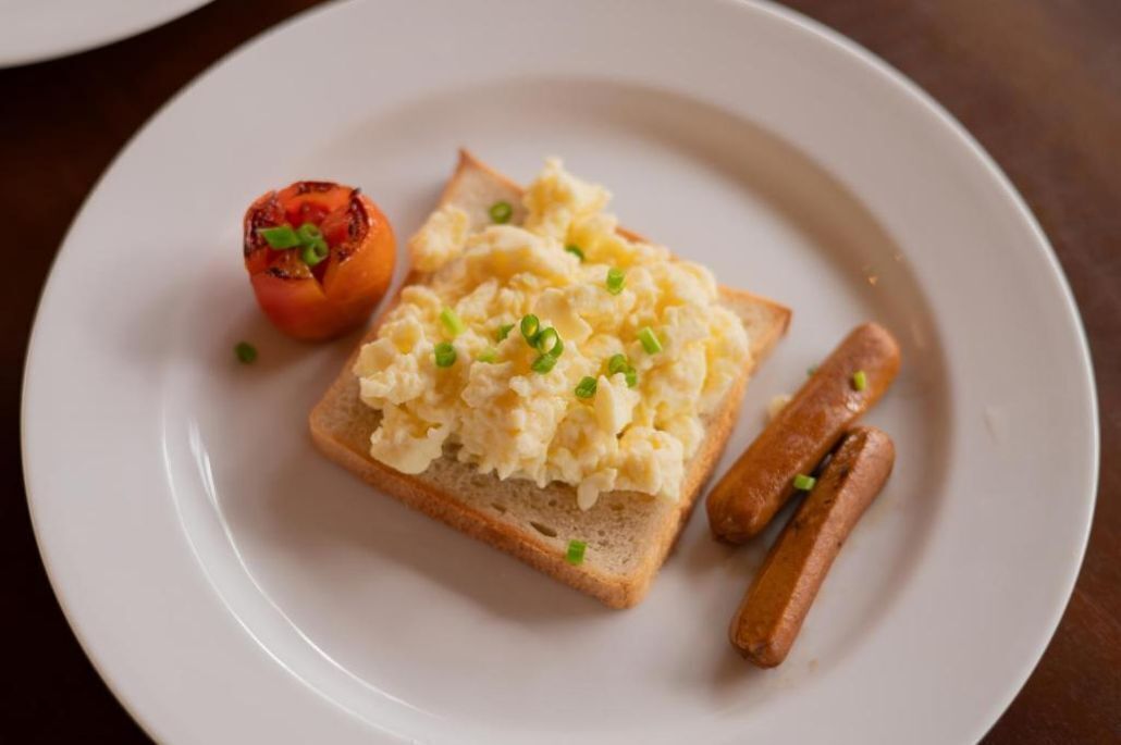 Une assiette avec des œufs brouillés sur des toasts, une tomate grillée et deux saucisses.