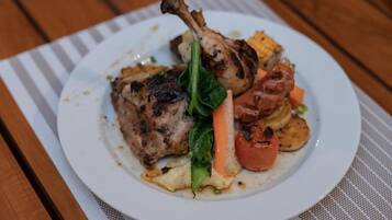 A plate of food with a grilled chicken leg, vegetables, and a slice of bread.