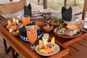 Mesa de madeira com uma mesa de café da manhã, incluindo frutas, pão e um copo de suco de laranja.