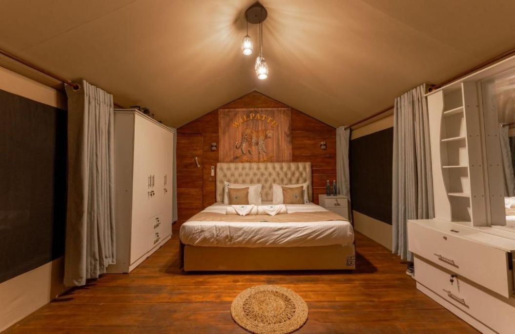 A bedroom with a wooden ceiling, a bed with a headboard, a bedside table, a wardrobe, and a window with curtains.