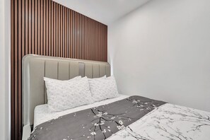 Ein modernes Schlafzimmer mit einem querverlegten Holz-Kopfteil, einem grau gepolsterten Kopfteil und einer Bettdecke mit Blumenmuster.