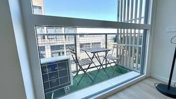 Un balcón con vistas a edificios, una mesa, sillas y un equipo de aire acondicionado.