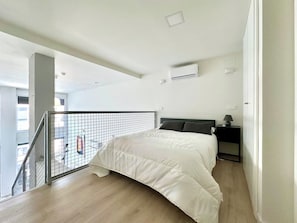 Une chambre à coucher comprenant un lit, une table de chevet, un appareil de climatisation et une fenêtre donnant sur l’extérieur.