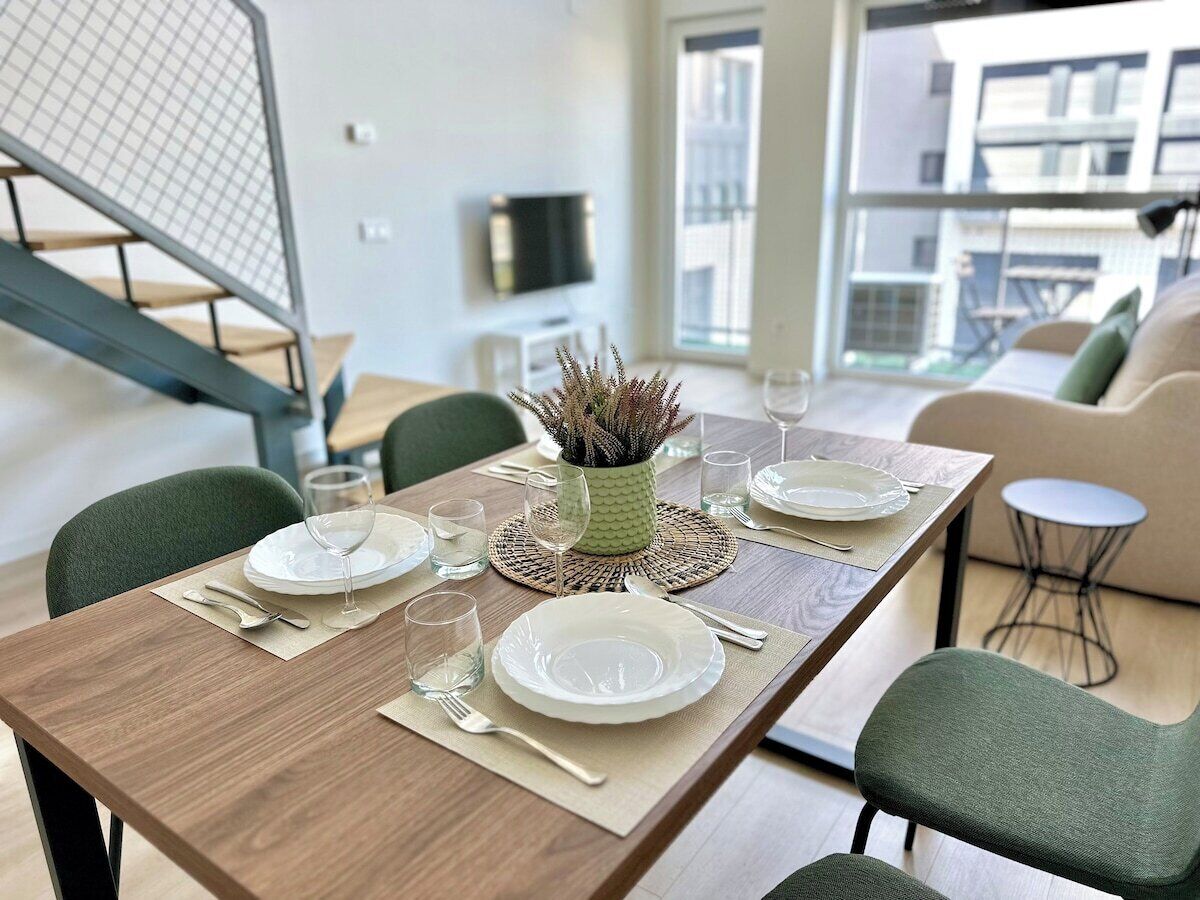 Un coin repas avec une table en bois mise pour quatre personnes, comprenant des assiettes, des couverts et des verres.