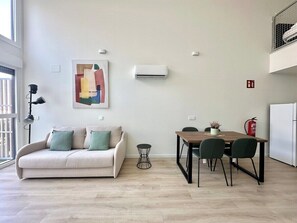 Un salon moderne comprenant un canapé, une table à manger avec des chaises, une petite table d’appoint et un climatiseur fixé au mur.