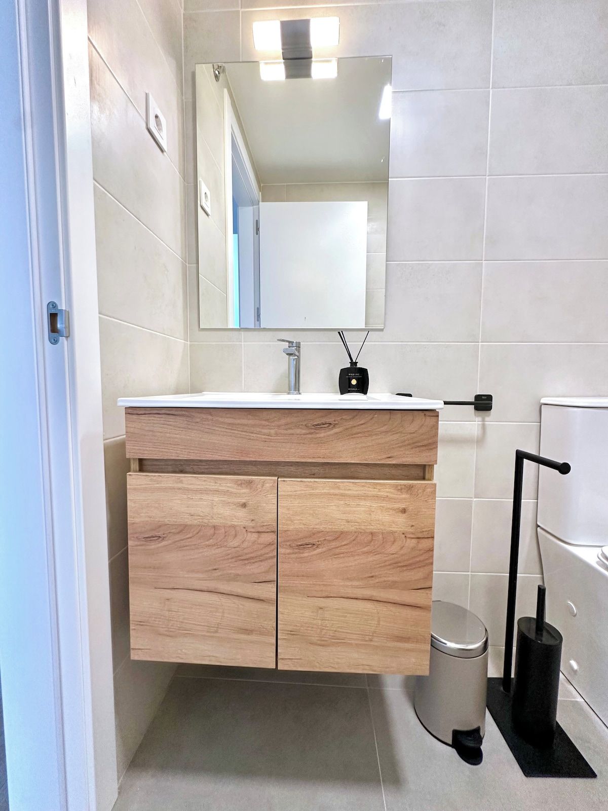 Un baño moderno con tocador de madera, espejo, inodoro y cubo de basura.