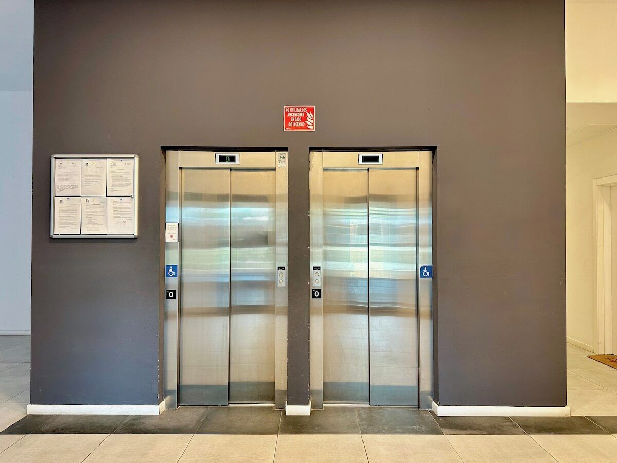 A pair of elevator doors with a sign above them and a notice board to the left.