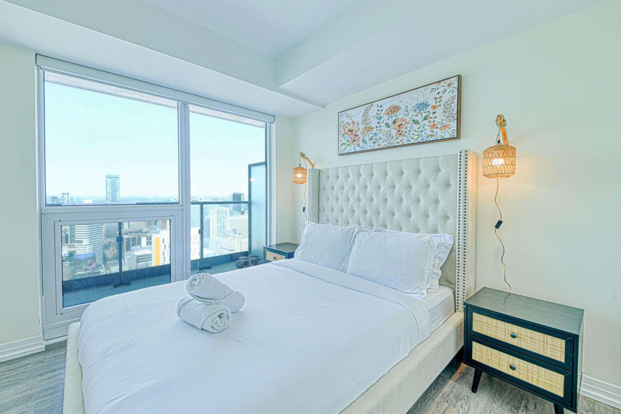 Quarto com cama grande, vista para a cidade, um objeto decorativo na parede e duas luminárias fixadas.