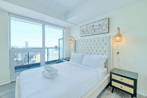 Une chambre avec un grand lit, une vue sur la ville, un élément décoratif mural et deux lampes fixées au mur.