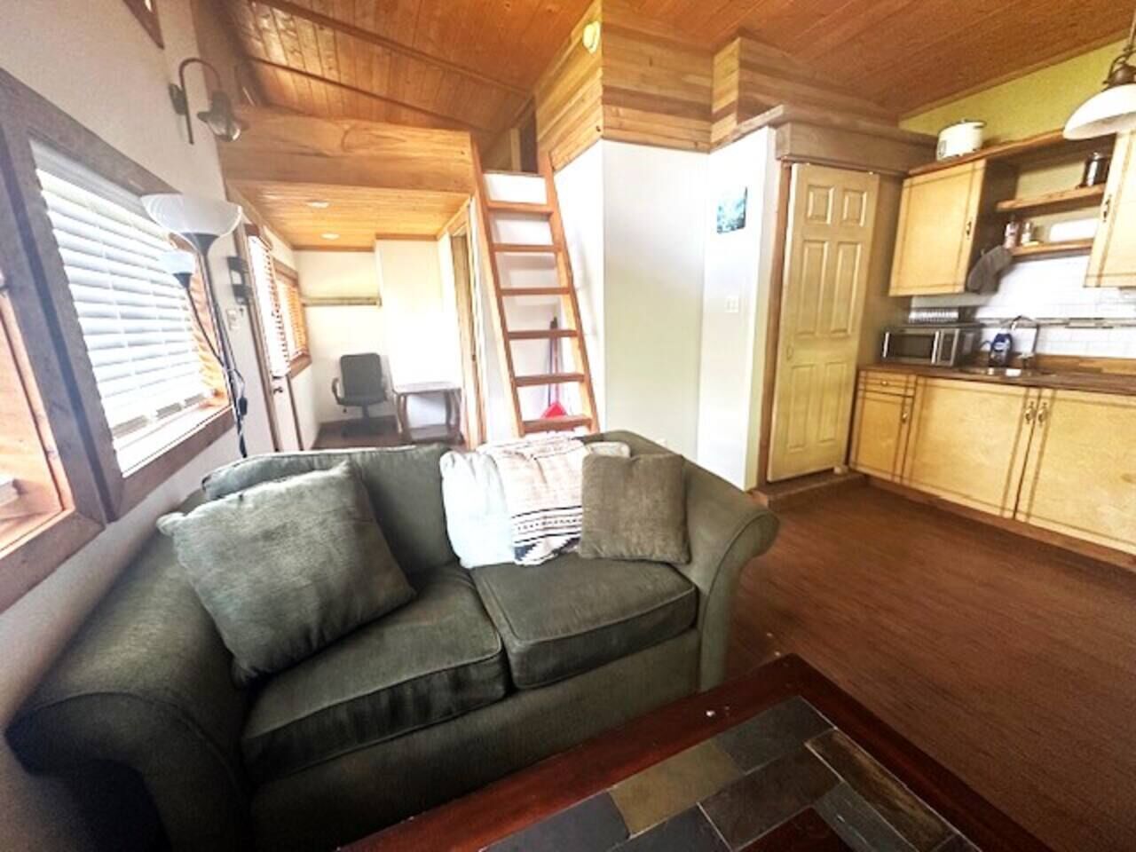 A cozy living area with a sofa, a ladder, and a kitchen with wooden cabinets.