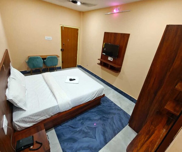 A hotel room with a bed, a desk, a chair, a television, and a door.
