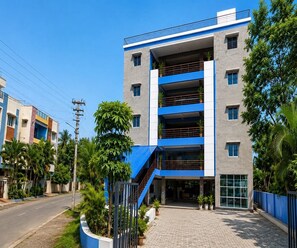 A multi-story building with a blue and white facade, a central staircase, and a paved entrance area. - Standard Room Pratikshya & Pratistha (Balianta)