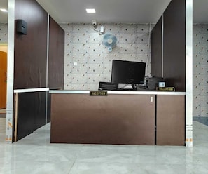 A reception desk with a computer, a fan, and a sign labeled 'RECEPTION'. - Standard Room Pratikshya & Pratistha (Balianta)