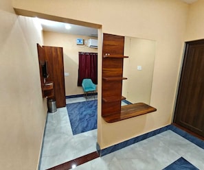 A room with a wooden shelf unit, a blue chair, and a tiled floor with a marble pattern. - Standard Room Pratikshya & Pratistha (Balianta)