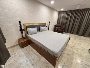 Un dormitorio con una cama grande, una mesita de noche, una silla y una cortina.