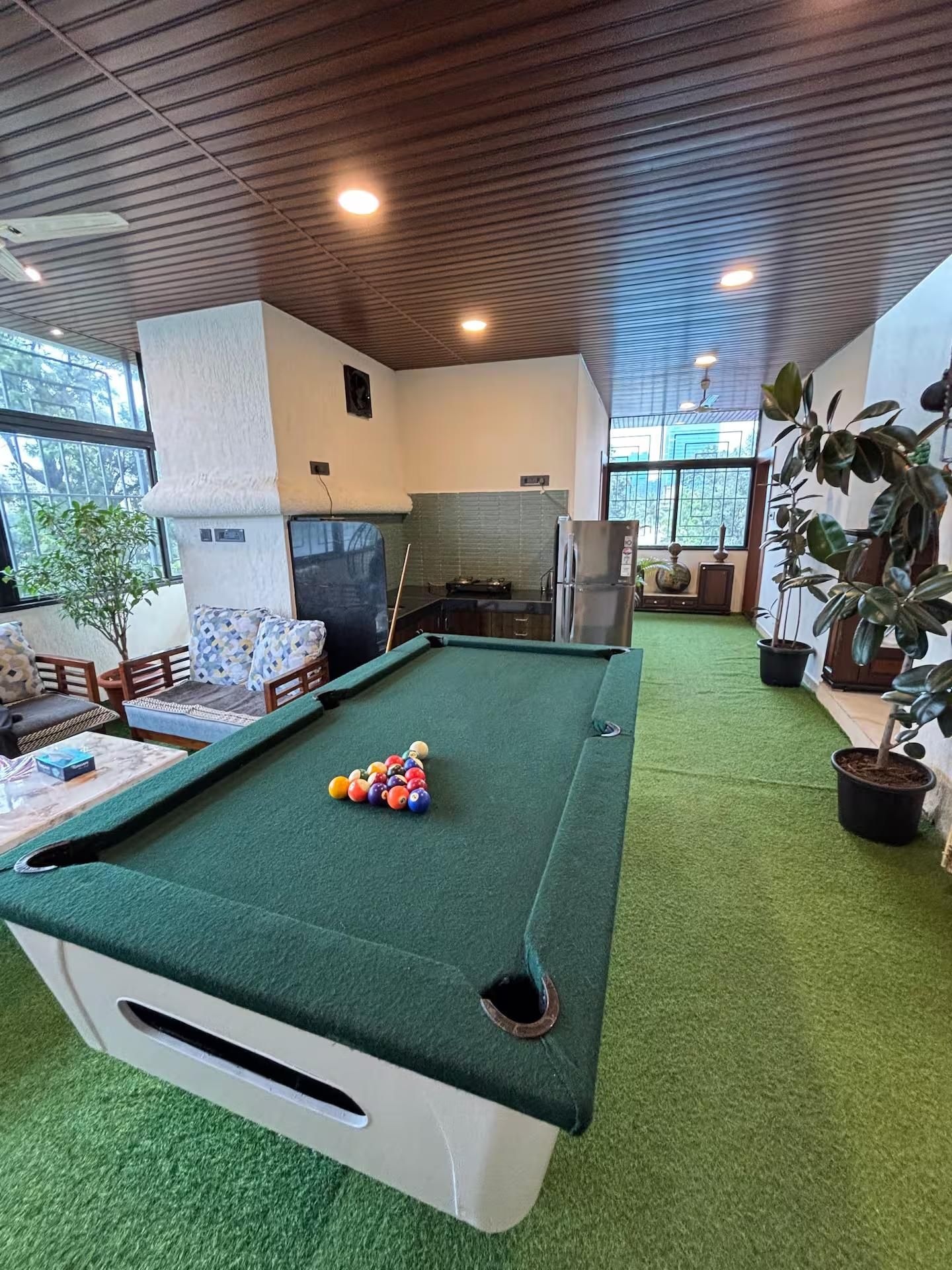Een pooltafel met ballen, een bank, een eethoek en potplanten.
