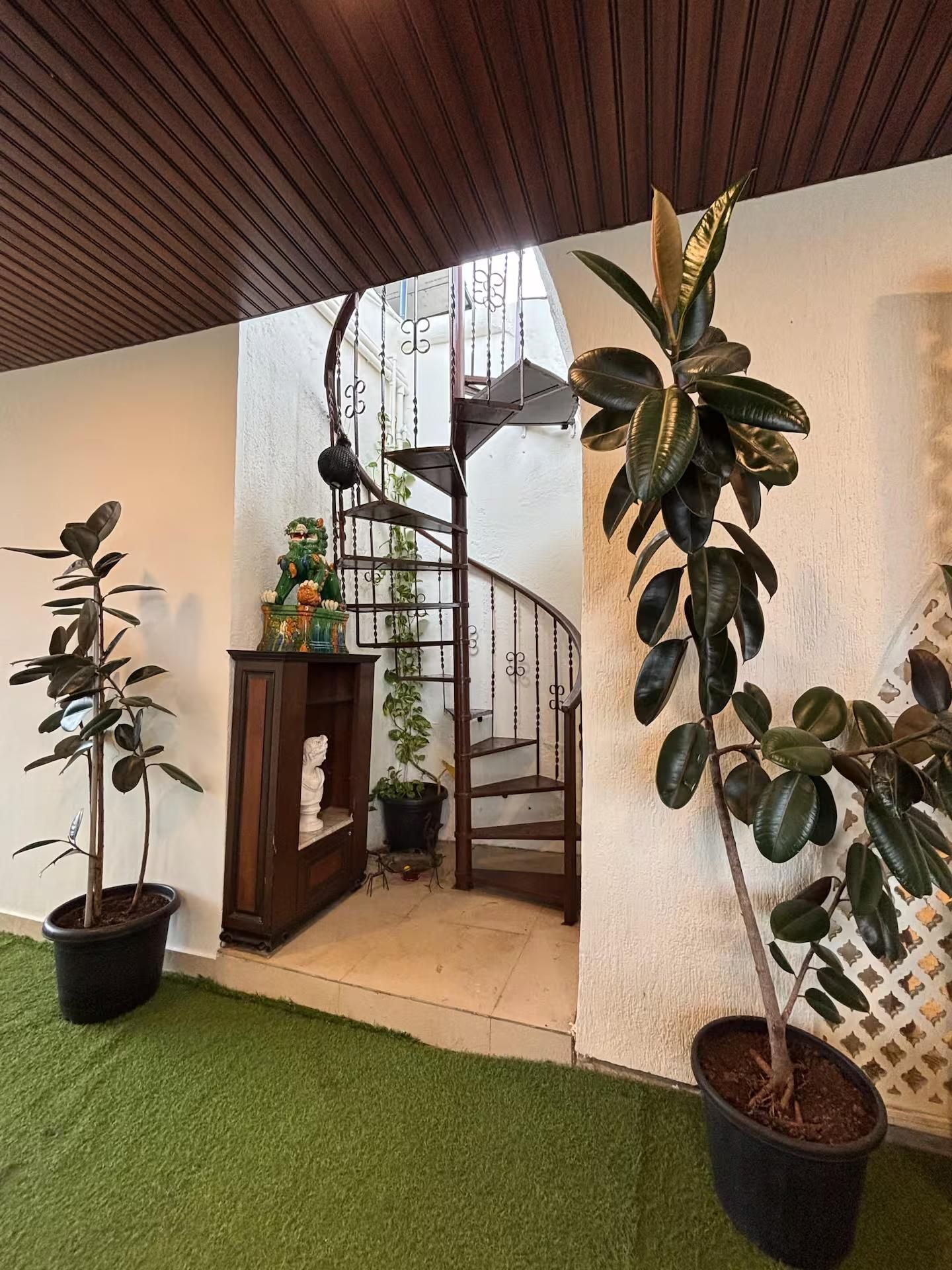 Een wenteltrap, omringd door potplanten en een houten kast.