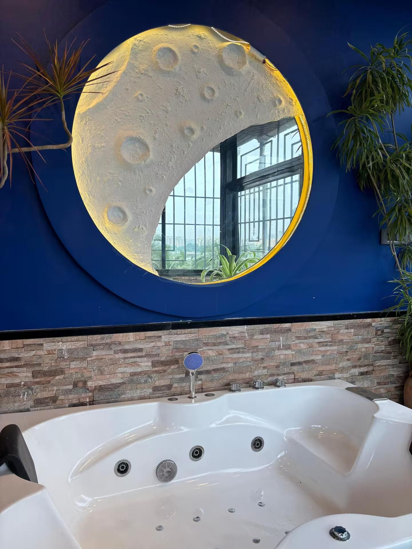 A bathroom with a large circular mirror, a bathtub, and a window.