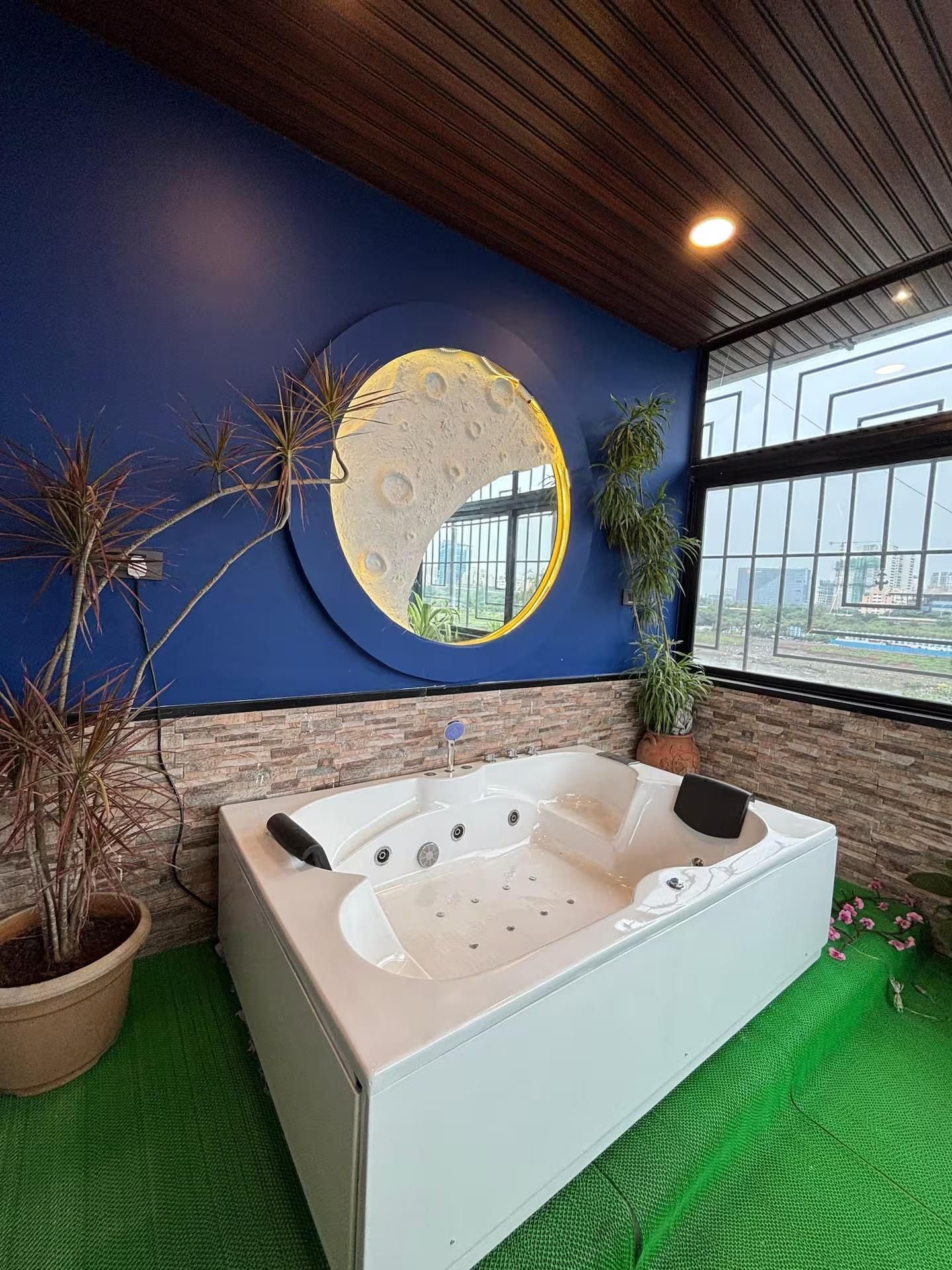 Een moderne badkamer met een groot bad, een ronde maan muurschildering en uitzicht op de stad door grote ramen.