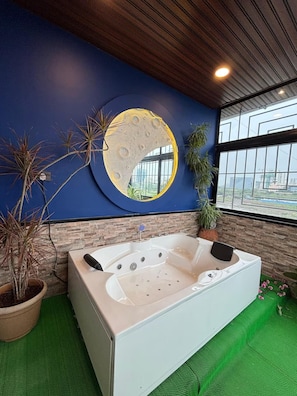 Een moderne badkamer met een groot bad, een ronde maan muurschildering en uitzicht op de stad door grote ramen.
