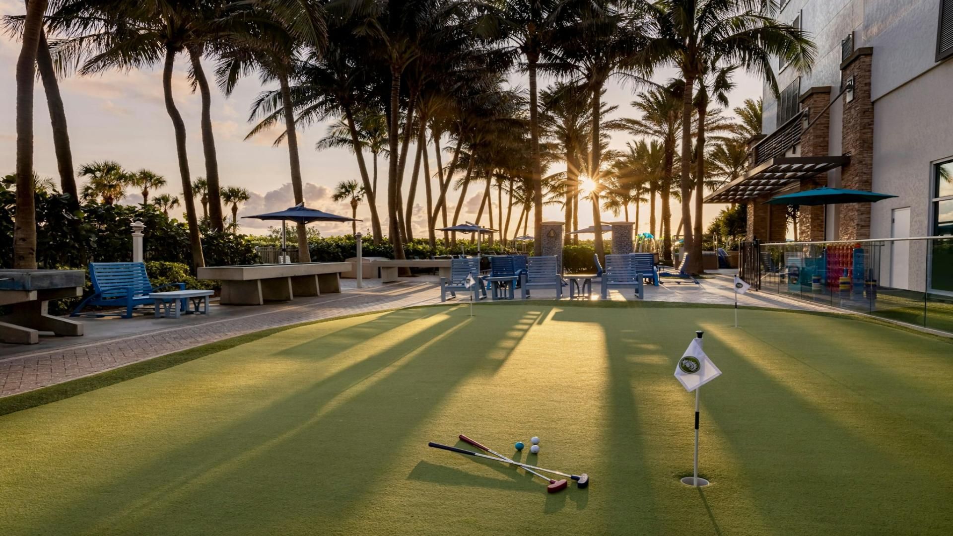 A golf course with a putting green, lounge chairs, and palm trees.