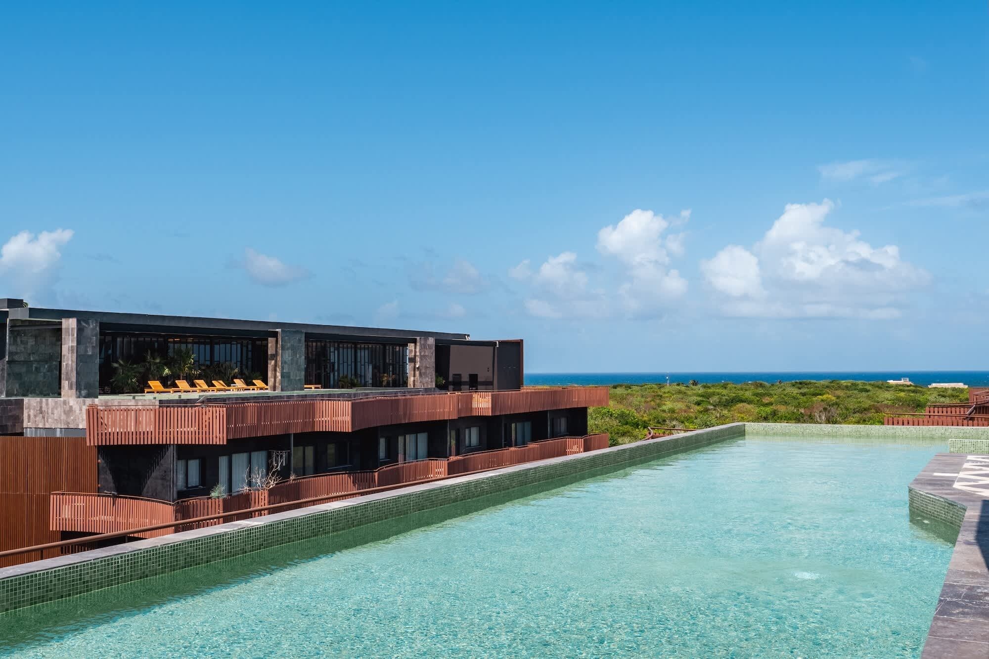 A modern hotel with a swimming pool, a view of the ocean, and a tropical landscape.