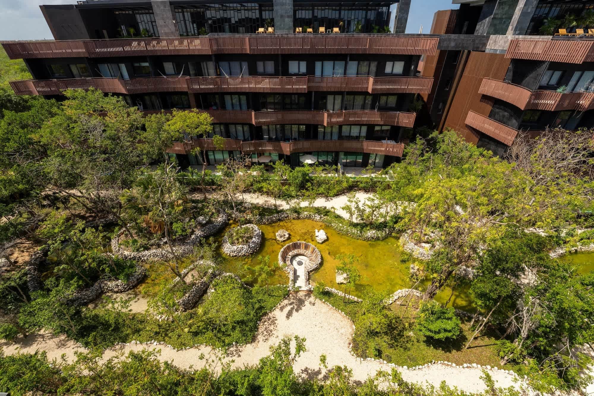 A modern building with multiple balconies and a landscaped garden with a central water feature.
