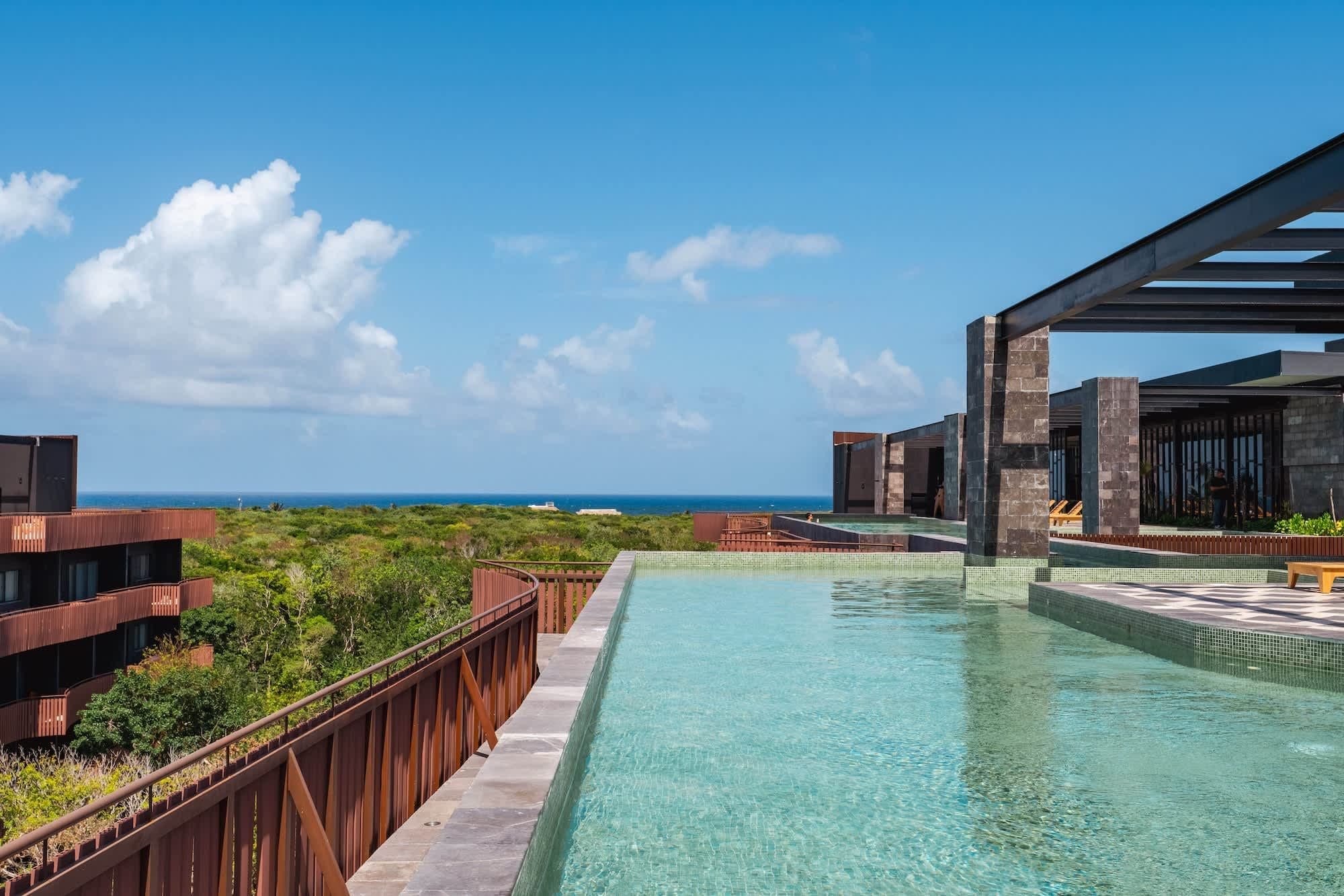 Una piscina con vista sull'oceano, circondata da architettura moderna e rigogliosa vegetazione.