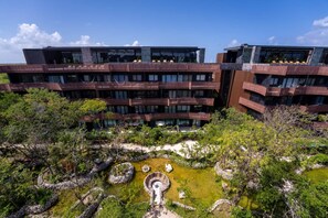 A modern multi-story building with balconies, surrounded by a landscaped garden with a central water feature. - Stylish Amira District Studio w/ shared Pool & Gym (Tulum)