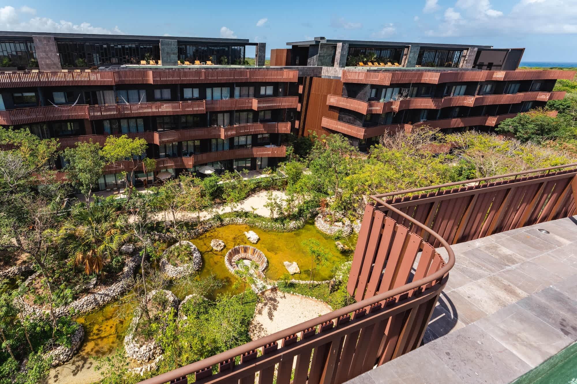 A modern building with multiple balconies overlooking a landscaped area with a pond.