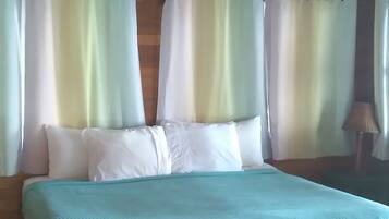 A bed with a teal bedspread in a room with wooden ceiling beams and a tiled floor.