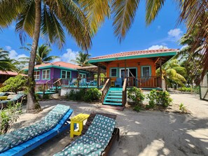 A beachfront property with multiple colorful cabins, a sandy beach, and palm trees. - Placencia Belize TWO cabanas on the sea with a pool! (Placencia)