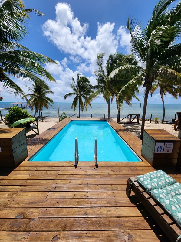 A wooden deck with a pool, palm trees, and a view of the ocean.