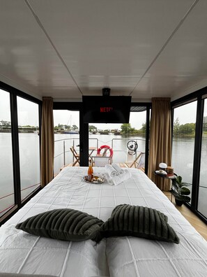 A room with a bed, a TV screen displaying 'NETFLIX', and a view of a body of water through large windows.