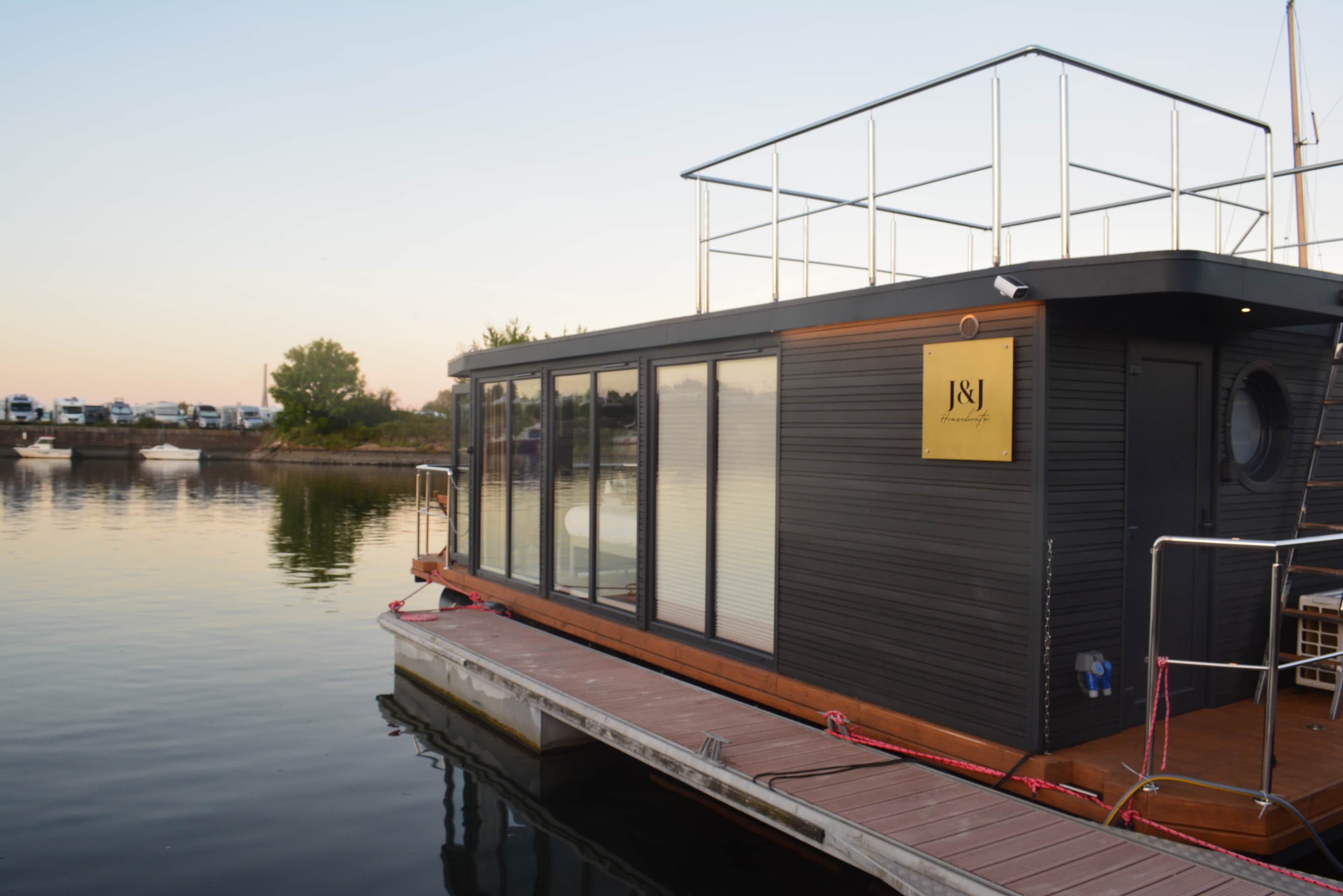 Barco estacionado com deck coberto, placa com a inscrição 'J&J Homebase' e um píer que se estende em águas calmas.