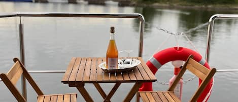 A wooden deck with a table and chairs, a bottle of wine, and a life ring.