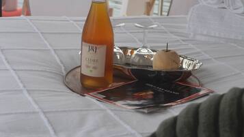 Ein Tisch mit einer Flasche J&J Wein, einem Glas und einer Schale mit einem Holzgegenstand, vor dem Hintergrund von Wasser und dem Steuerrad eines Bootes.