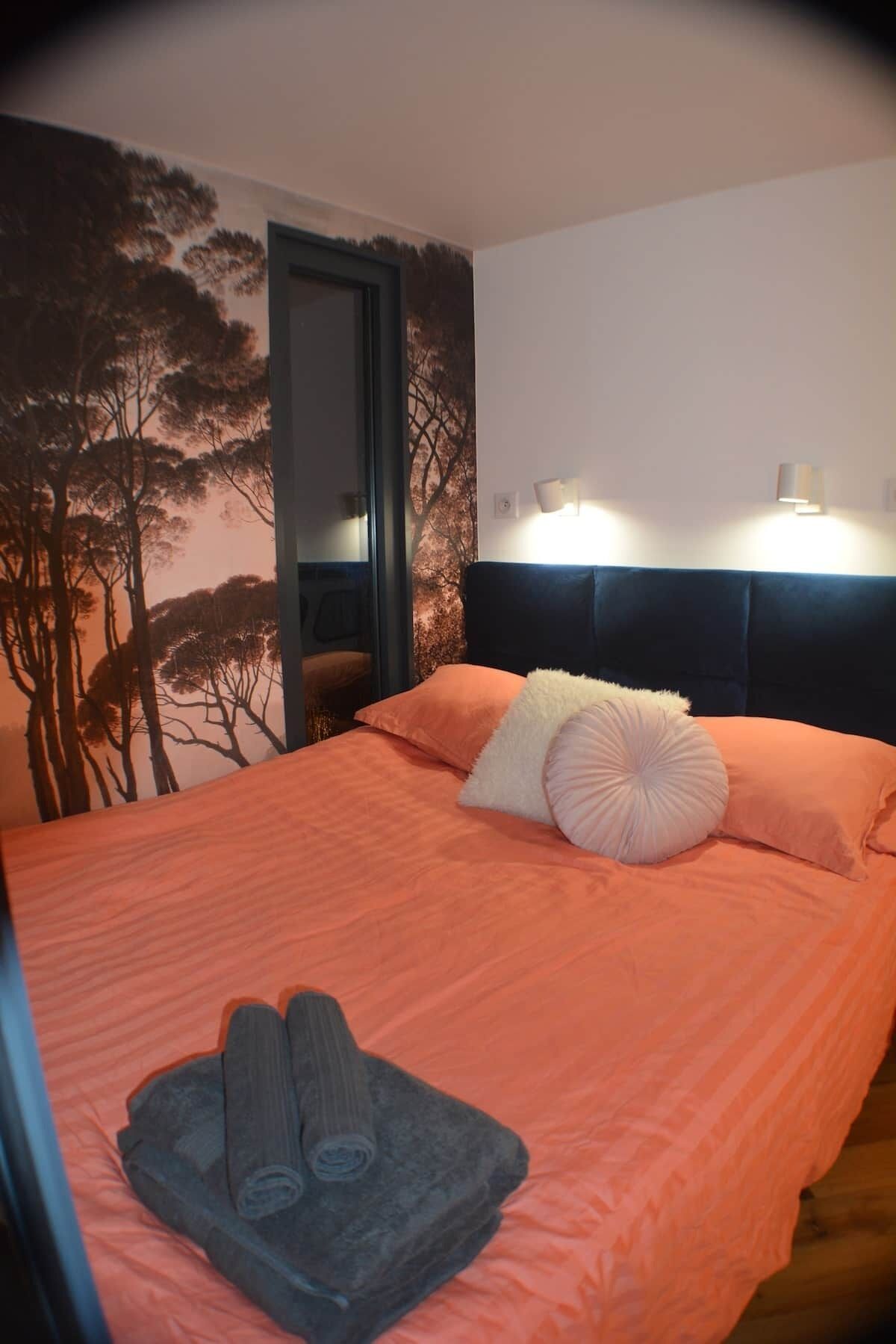 Habitación de hotel con cama, cabecera, pared con un mural de un árbol y dos luces fijadas a la pared.