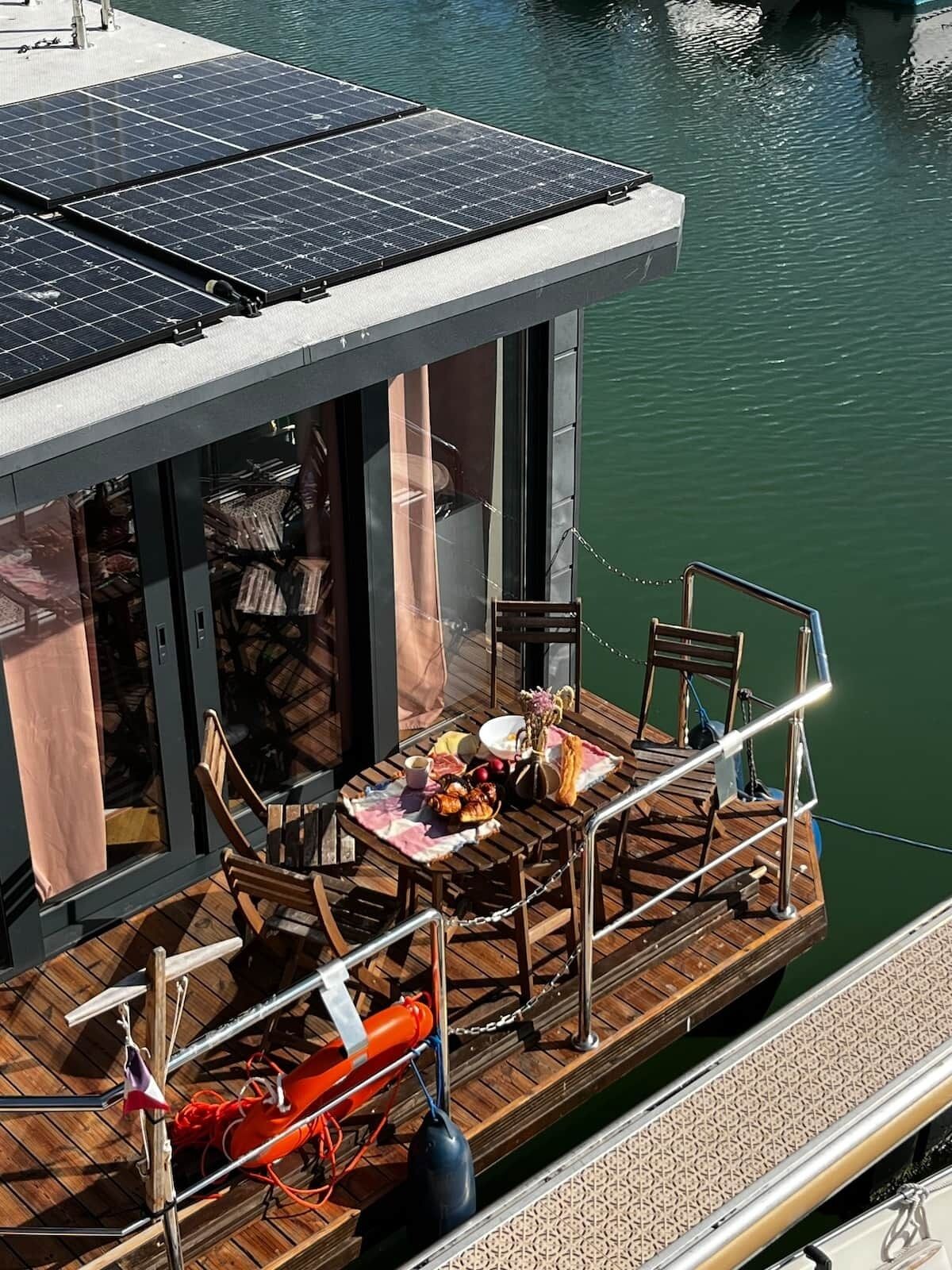 Un restaurante flotante con comedor, sillas, mesa dispuesta con comida y paneles solares en el techo.