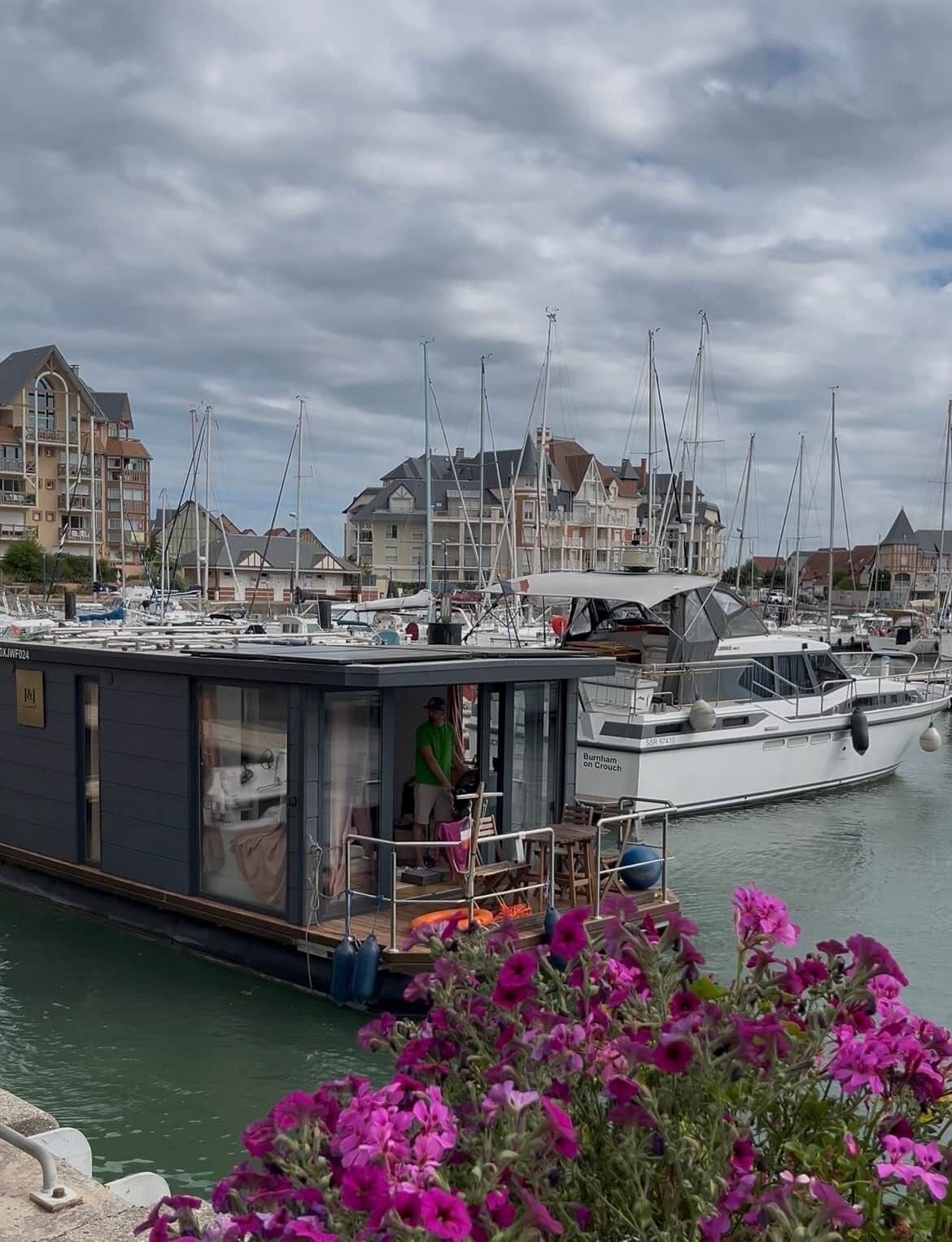 Un puerto deportivo con barcos amarrados, un edificio con balcón y una persona de pie en el muelle.