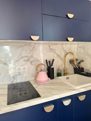 A kitchen with a marble countertop, a sink, a kettle, and a set of knives.