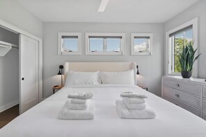 Ein Hotelzimmer mit einem großen Bett, zwei Nachttischen, einem Kleiderschrank und drei Fenstern.