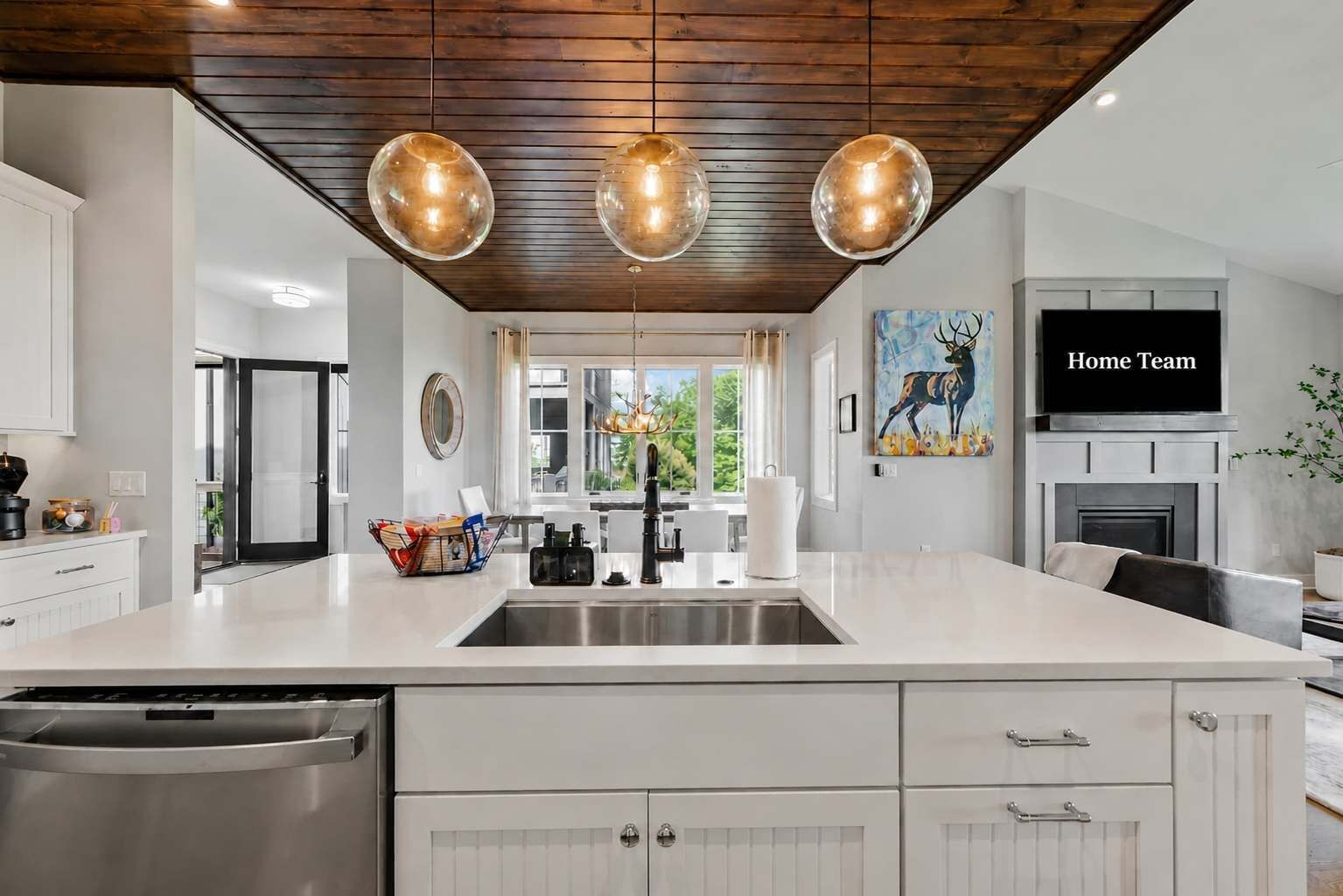 A modern kitchen with a large island, stainless steel appliances, pendant lighting, and a painting of a deer.