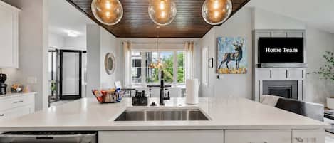 A modern kitchen with a large island, stainless steel appliances, pendant lighting, and a painting of a deer.