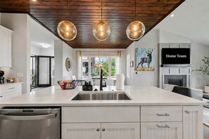 Une cuisine moderne dotée d’un grand îlot central, d’appareils électroménagers en acier inoxydable, de luminaires suspendus et d’un tableau représentant un cerf.