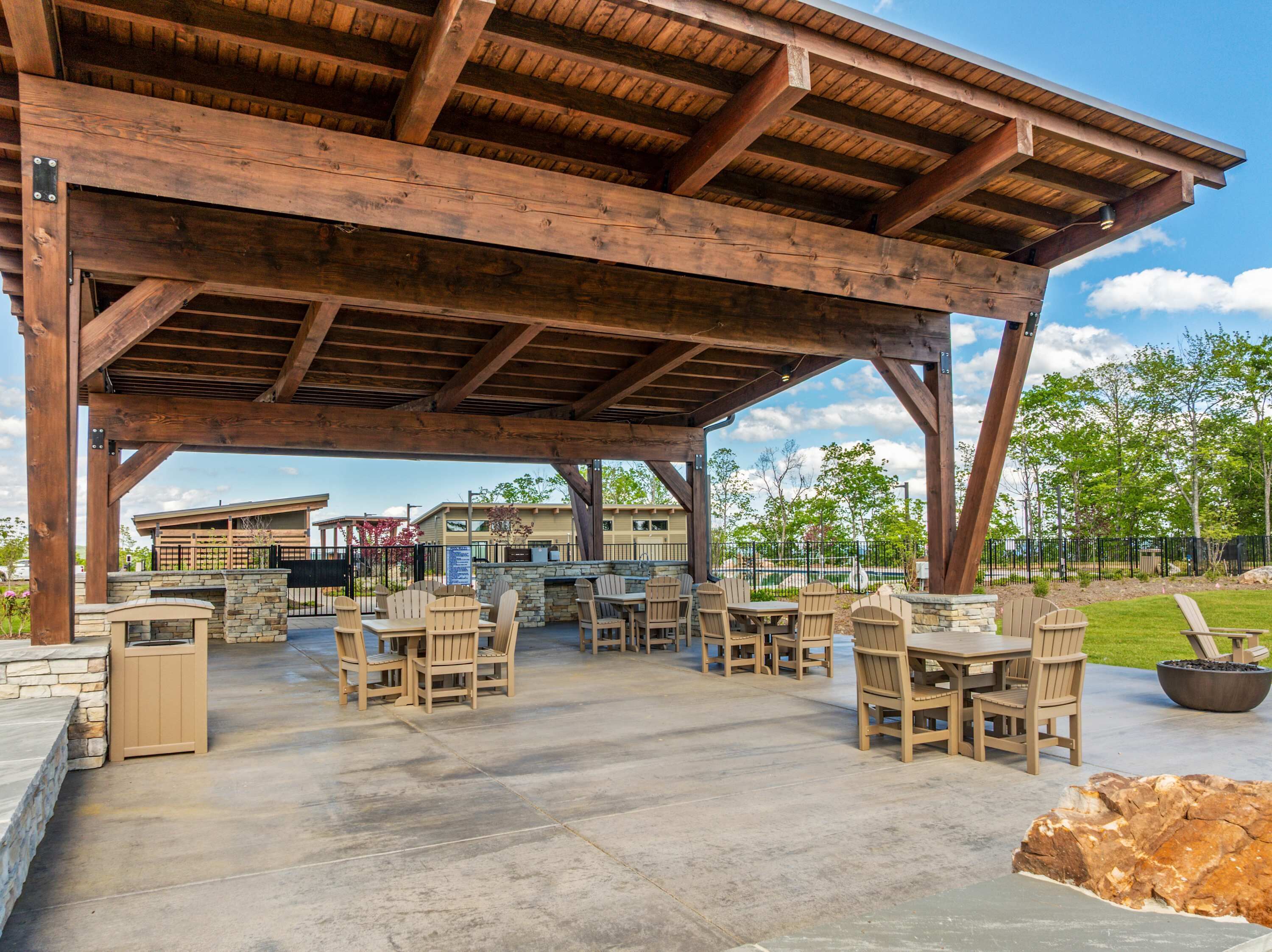 An outdoor patio with wooden tables and chairs, stone walls, and a view of a residential area.
