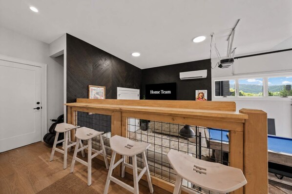 Une pièce comprenant un coin bar, quatre tabourets, une porte et une fenêtre donnant sur un paysage agréable.