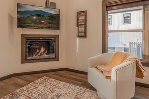 A living room with a fireplace, a television mounted on the wall, a framed sign, and a window. - Cove Reserve | Brand New | Sleeps 14 | Top 10% (Sevierville)