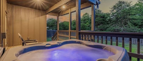 Un jacuzzi en una terraza de madera con vistas a árboles y al atardecer.