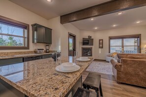 A modern kitchen with granite countertops, a dining area with a bench, and a living room with a sofa. - Cove Reserve | Brand New | Sleeps 14 | Top 10% (Sevierville)